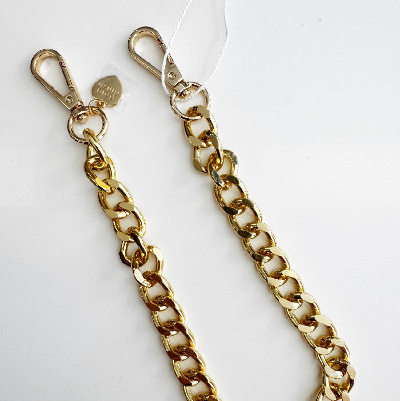 A shiny gold tone acrylic bag chain strap featuring large oval links, dual secure lobster clasps, and a decorative heart charm on a clean white background.