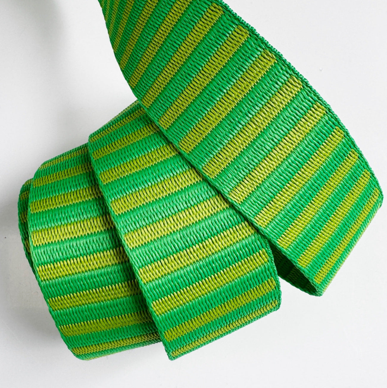 A 1.5-inch wide jacquard woven webbing strap featuring a vibrant green and lime yellow horizontal stripe pattern, neatly coiled against a white background.