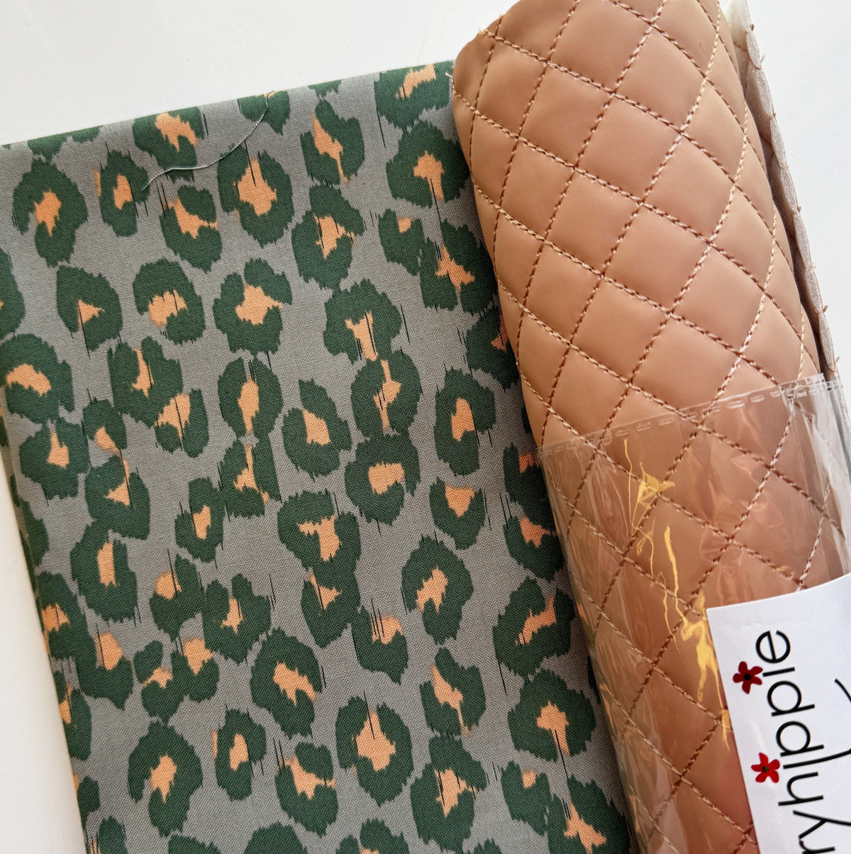 Bag-making fabric set featuring green-gray cotton fabric with a forest green and peach-tan abstract ikat leopard print, paired with camel-brown diamond-quilted faux leather vinyl in protective plastic wrapping. Coordinating cotton quilting fabric and quilted vinyl for handmade handbags, purses, tote bags, and DIY sewing projects.