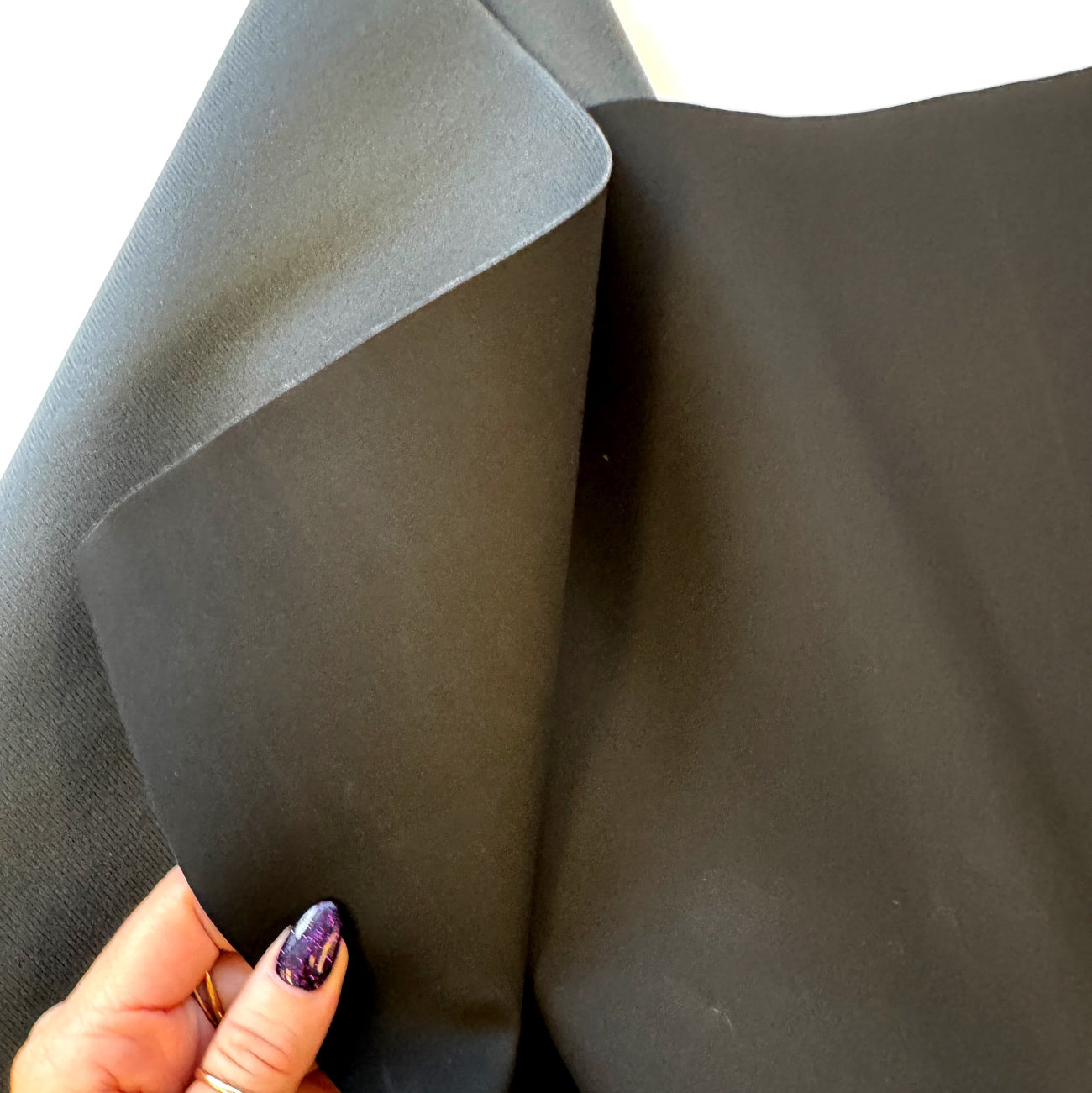 A close-up view of a hand holding the matte black fabric, highlighting its smooth surface.