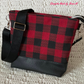A handmade crossbody bag featuring a red and black buffalo plaid fabric body, a textured black pebbled faux leather base, silver metal hardware adjusters, and an adjustable black geometric diamond jacquard webbing shoulder strap