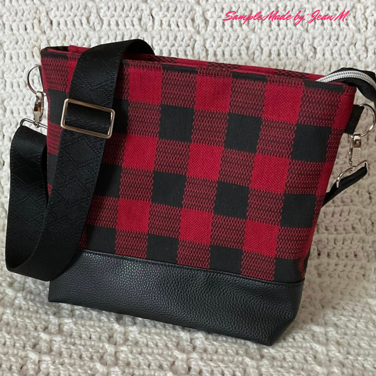 A handmade crossbody bag featuring a red and black buffalo plaid fabric body, a textured black pebbled faux leather base, silver metal hardware adjusters, and an adjustable black geometric diamond jacquard webbing shoulder strap