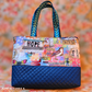 Handmade fabric tote bag featuring a colorful bird and dragonfly collage print with inspirational words like HOPE and SOAR, a dark navy blue diamond-quilted vinyl base, and blue-green leaf-patterned ribbon shoulder straps. Bag handmade by Sandie N.