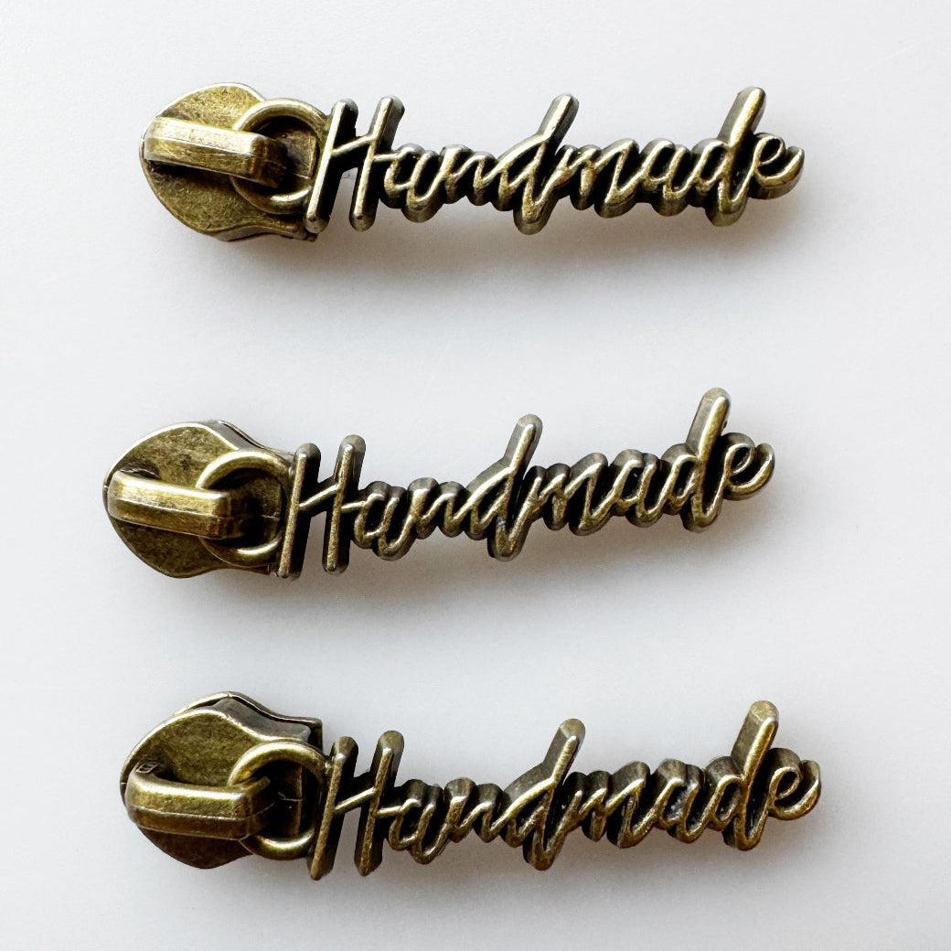 Three identical antique bronze metal zipper pull charms spelling out 'Handmade' vertically on a clean white background.