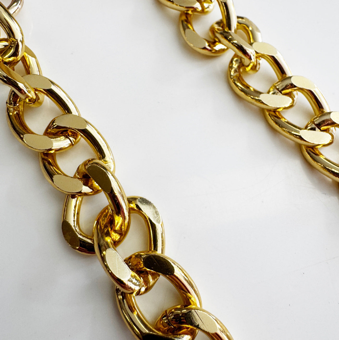 Angled view of two parallel rows of a chunky gold tone acrylic chain showing smooth polished oval links on a white background.