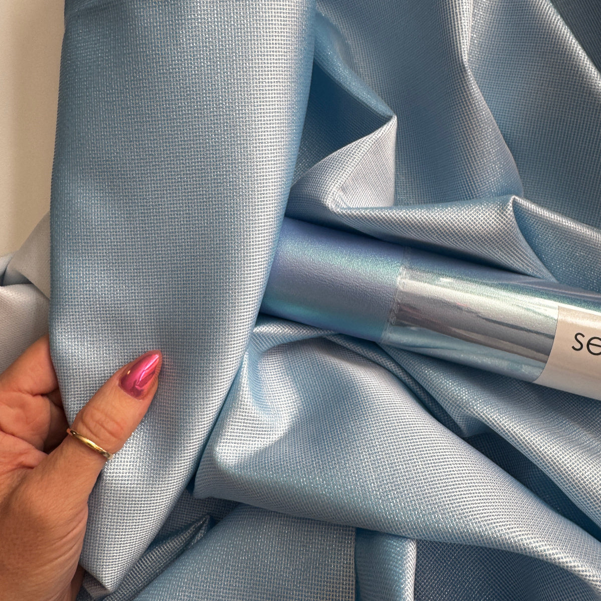 Hand holding light blue satin fabric with a visible brand name.