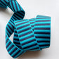 A close-up of a striped elastic ribbon or trim coil on a plain white background. The ribbon features alternating horizontal stripes of bright turquoise blue and dark navy blue.