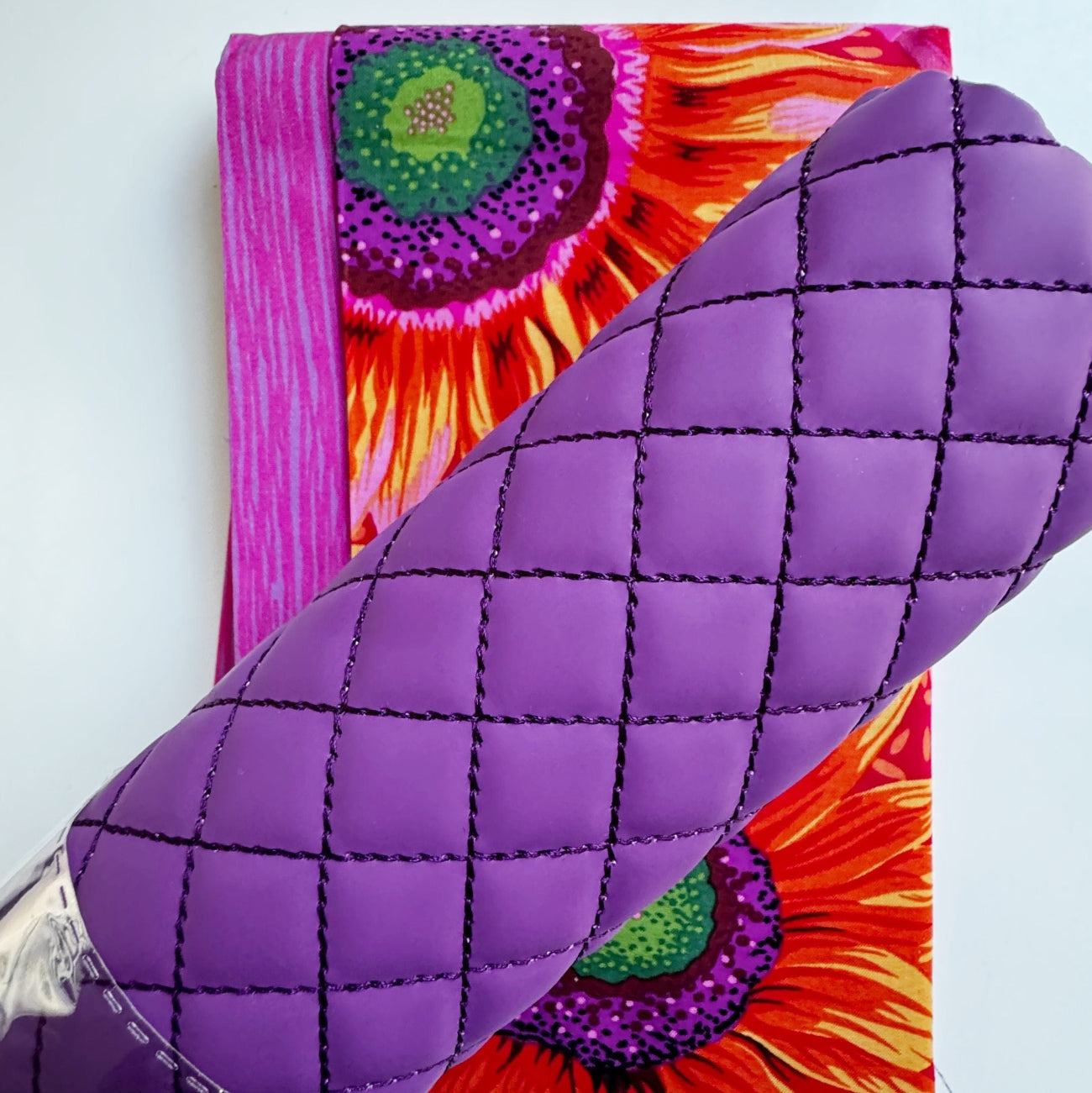 A close-up of a purple quilted leather accessory, likely a clutch or small bag, with a vibrant floral print backing visible underneath.