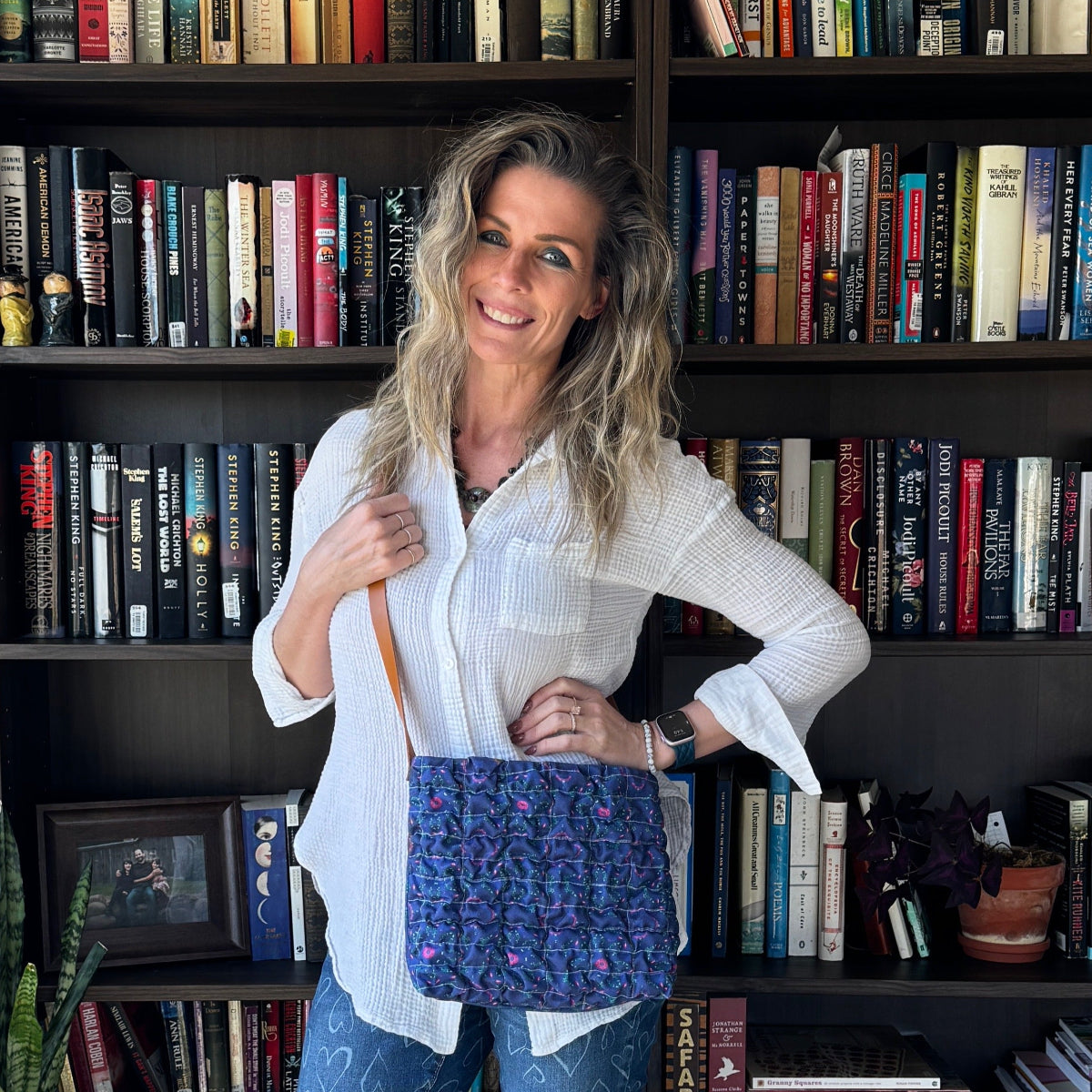 Woman holding a blue bag in front of a bookshelf