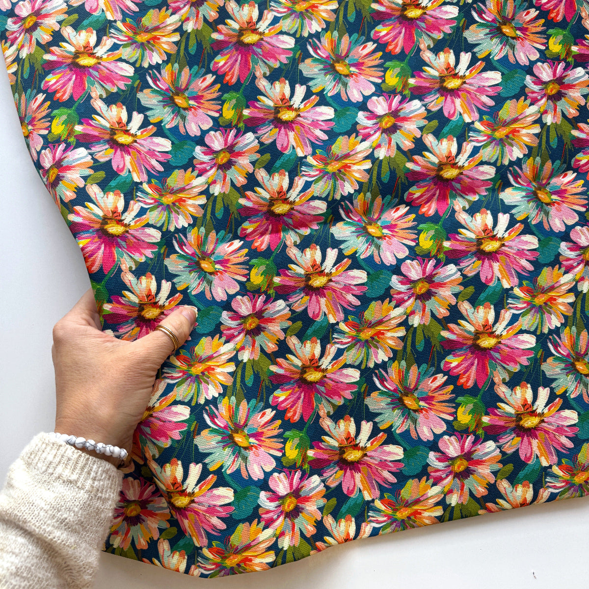 Hand holding a piece of fabric with colorful floral pattern on a white background