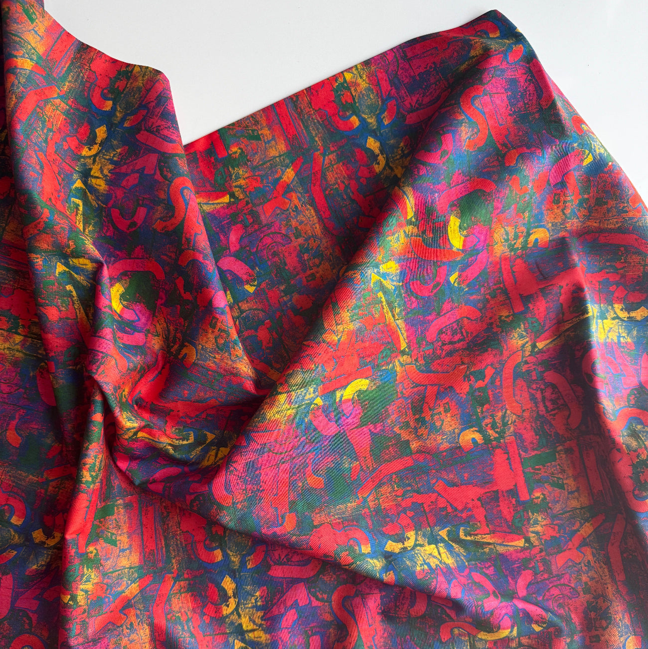 Draped abstract fabric featuring a vibrant, multi-colored graffiti-style pattern in shades of red, blue, yellow, and green.
