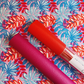 Lipstick pink and orange Moonglow vinyl rolls displayed on coordinating floral canvas fabric, ideal for handbags, wallets, totes, bag making, sewing, and DIY craft projects.