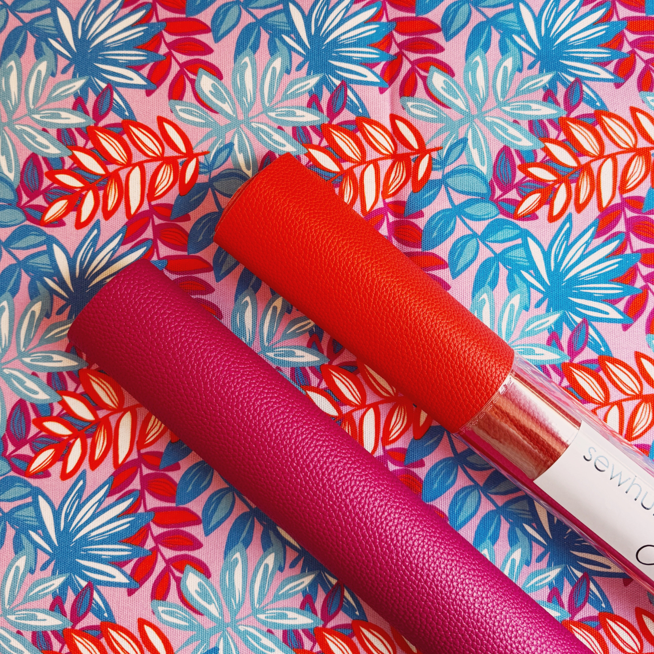 Lipstick pink and orange Moonglow vinyl rolls displayed on coordinating floral canvas fabric, ideal for handbags, wallets, totes, bag making, sewing, and DIY craft projects.