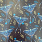 A seamless repeating pattern in the file luna moth vinyl roll 18 x 54.jpg featuring large, stylized blue luna moths on a dark charcoal-black background. The moths have intricate wing details showing moon phases and botanical leaves. The background is filled with scattered celestial elements like yellow crescent moons, tiny stars, faint sunbursts, glowing blue orbs, and small leafy sprigs in blue and yellow.