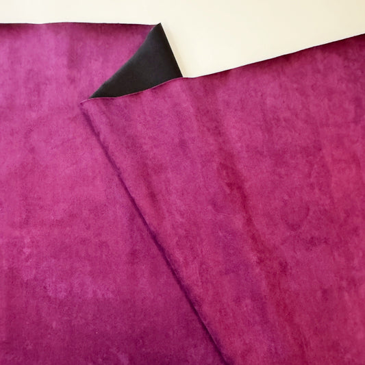 A folded piece of maroon fabric showing a velvety texture on one side and a smooth black lining on the other.