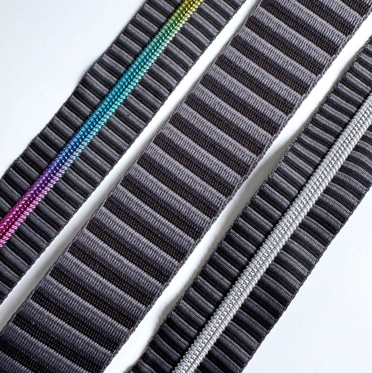 A charcoal grey and black striped bag making set featuring a continuous zipper tape with rainbow metallic coil teeth on the left, a thick matching jacquard woven webbing strap in the center, and a second zipper tape with metallic silver coil teeth on the right.