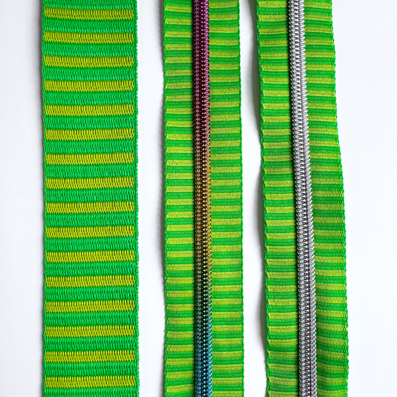 A green and lime yellow striped bag making set featuring a jacquard woven webbing strap on the left, a continuous zipper tape with rainbow metallic coil teeth in the center, and a matching zipper tape with silver coil teeth on the right.