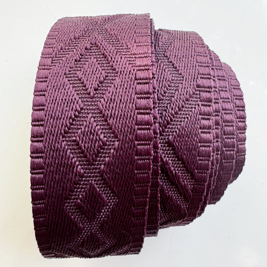 A side view roll of 1.5-inch wide premium jacquard woven webbing strap in a rich merlot wine color featuring an intricate diamond geometric pattern