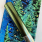 A roll of metallic green vinyl fabric resting on top of patterned blue and green forest-themed fabric.