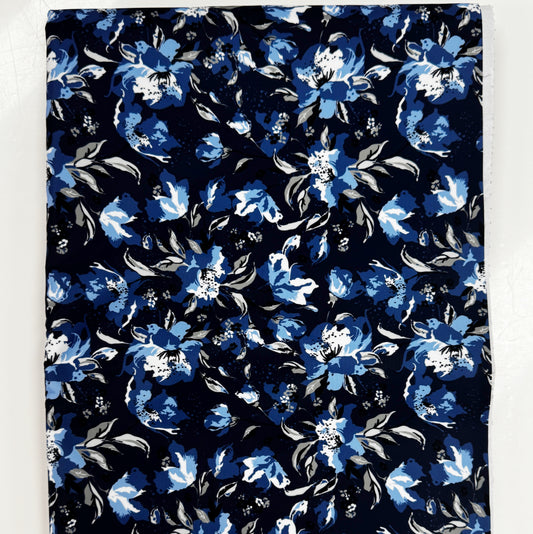 A flat, top-down view of the Midnight Bloom - Navy Blue Bonded Nylon – 36" x 58" fabric showing a rectangular piece of material. The navy blue bonded nylon fabric features a striking floral pattern with shades of light blue and white blossoms, layered alongside muted gray and white leaves. The dense, repeating botanical design is displayed clearly against a plain white background surface.