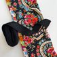 A sewing bundle featuring a folded vibrant floral fabric with red roses, blue blossoms, and multi-colored paisley borders on a black background, paired with a bundled roll of black jacquard woven webbing strap displaying a raised diamond geometric pattern.