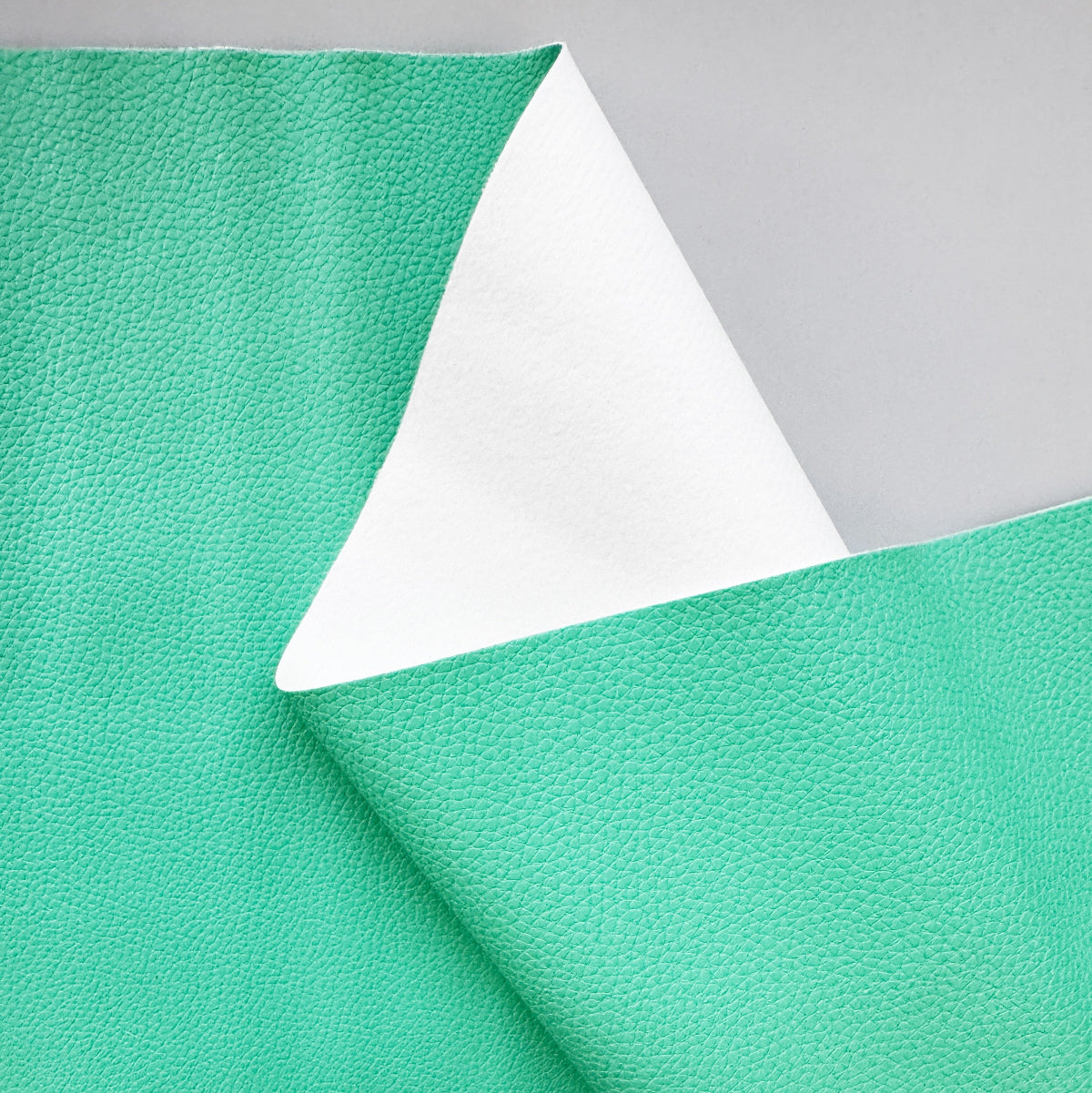 A close-up of a mint green textured material, showing its pebbled surface on one side and a smooth white reverse side on the folded corner, set against a light gray background.