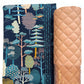 Moda quilting cotton fabric featuring the Feather and Forest Bloom Forest Trees print with whimsical teal, cream, gold, and peach trees on a midnight blue background, paired with dusty blush pink diamond-quilted faux leather vinyl. Coordinating bag-making materials for handmade handbags, quilted purses, and DIY sewing projects.