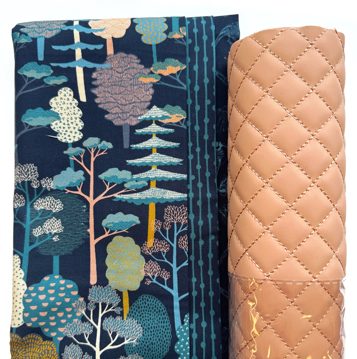 Moda quilting cotton fabric featuring the Feather and Forest Bloom Forest Trees print with whimsical teal, cream, gold, and peach trees on a midnight blue background, paired with dusty blush pink diamond-quilted faux leather vinyl. Coordinating bag-making materials for handmade handbags, quilted purses, and DIY sewing projects.