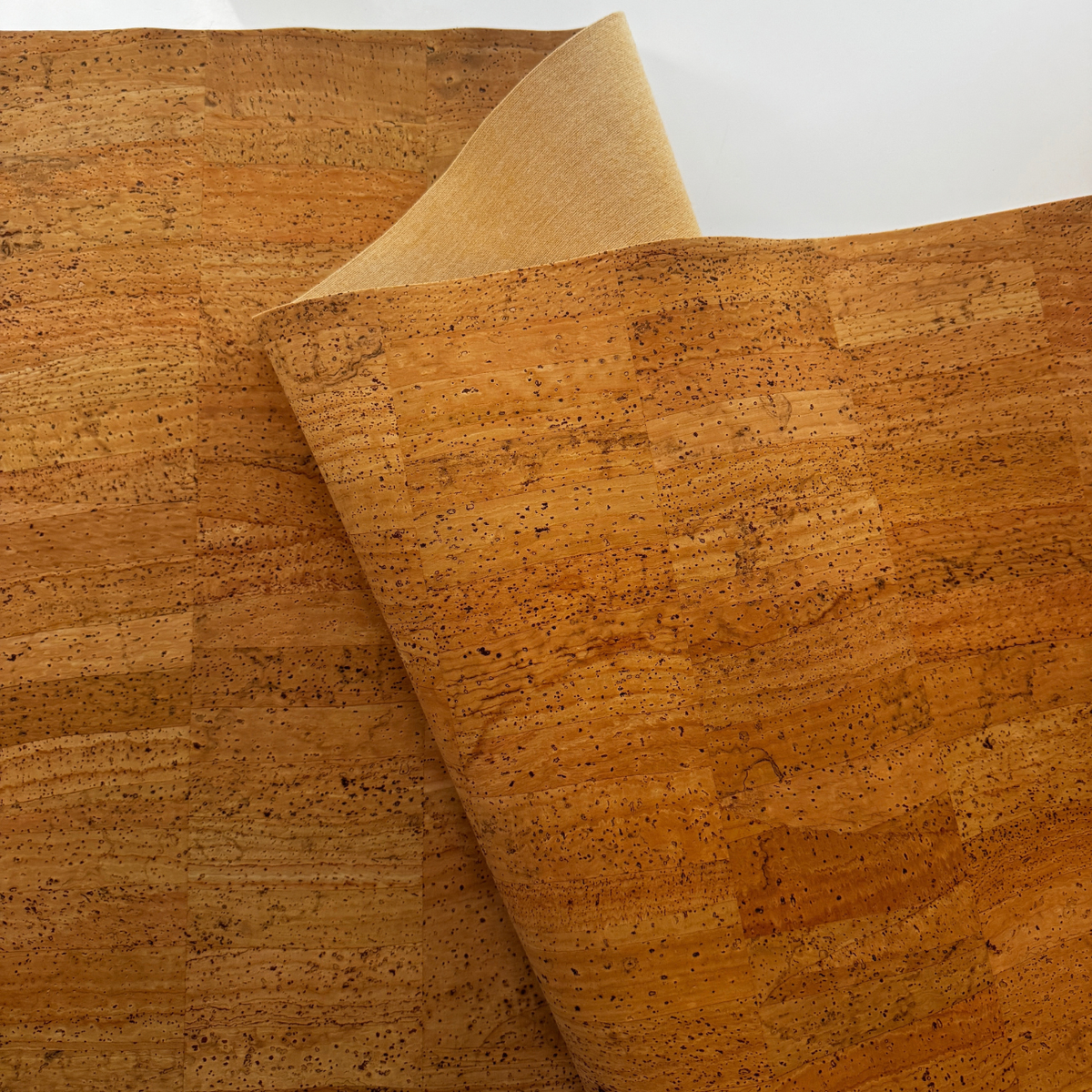 A close-up of cork wallpaper or a cork mat with a natural cork texture, showing a warm golden-brown color and a lighter tan backing sheet partially peeled back.