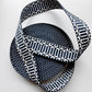 A coiled woven strap or ribbon with a navy blue and white geometric pattern, photographed on a clean white background.