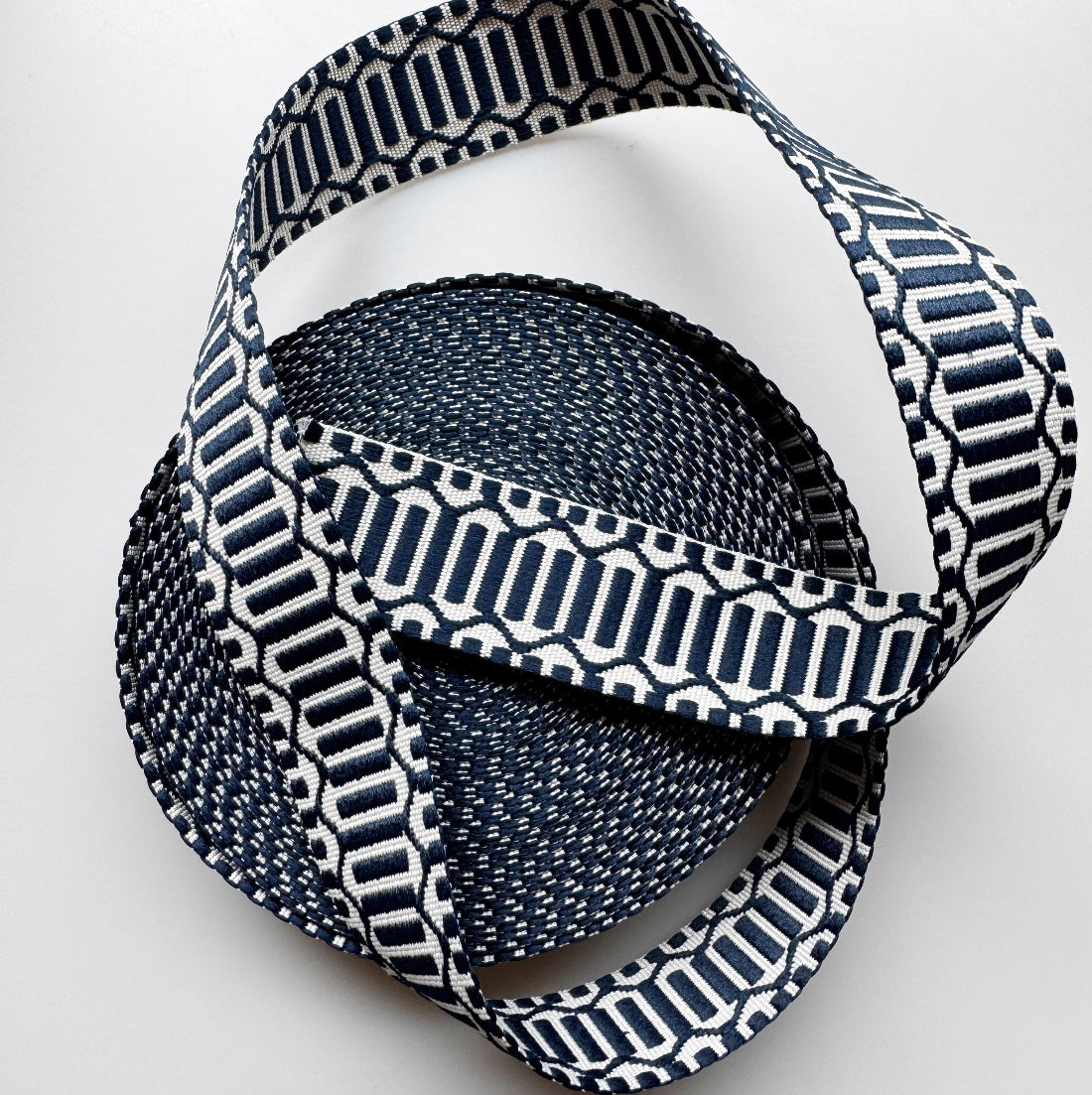 A coiled woven strap or ribbon with a navy blue and white geometric pattern, photographed on a clean white background.