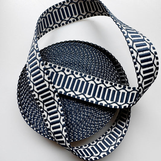 A coiled woven strap or ribbon with a navy blue and white geometric pattern, photographed on a clean white background.