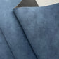 A close-up of folded blue textured material, likely fabric or leather, showing a mottled blue surface and a darker gray underside.