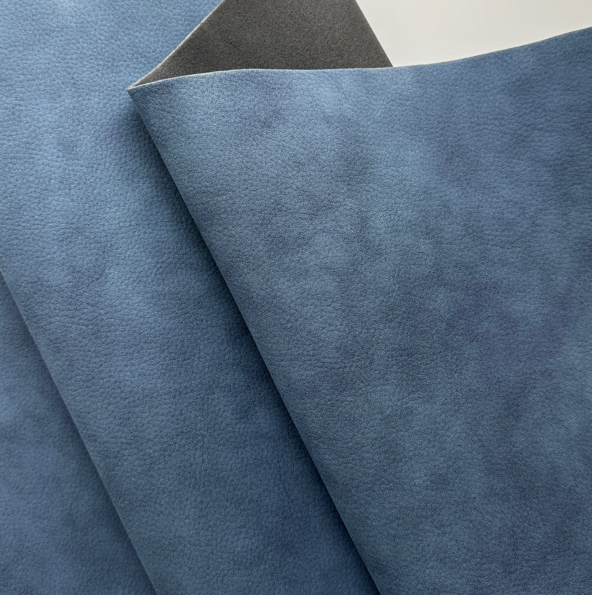 A close-up of folded blue textured material, likely fabric or leather, showing a mottled blue surface and a darker gray underside.