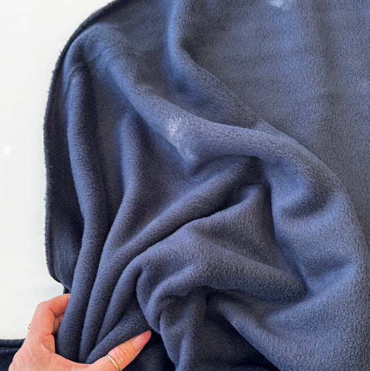 Close-up of a hand holding a dark blue fleece blanket against a white background