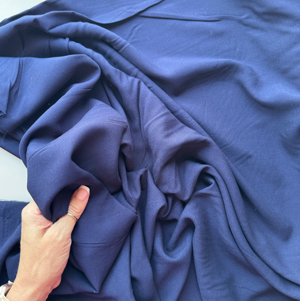 A close-up of draped navy blue fabric with a hand holding the material to show its drape and texture.