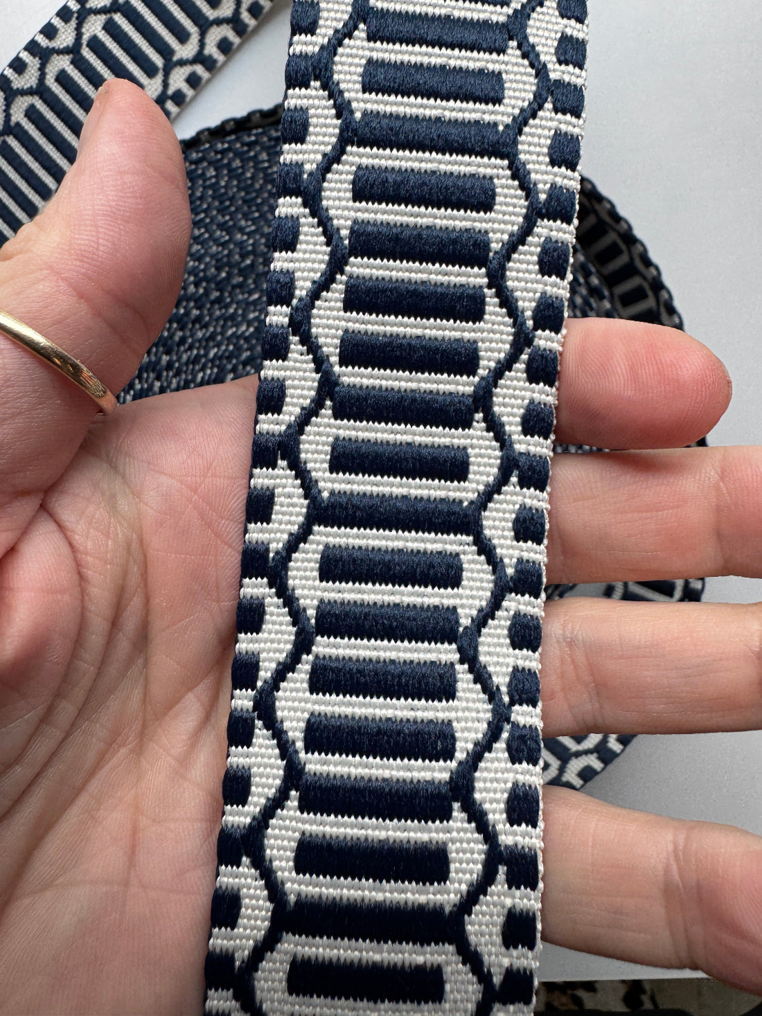 A close-up of a hand holding a woven fabric strap with a navy blue and off-white geometric pattern.