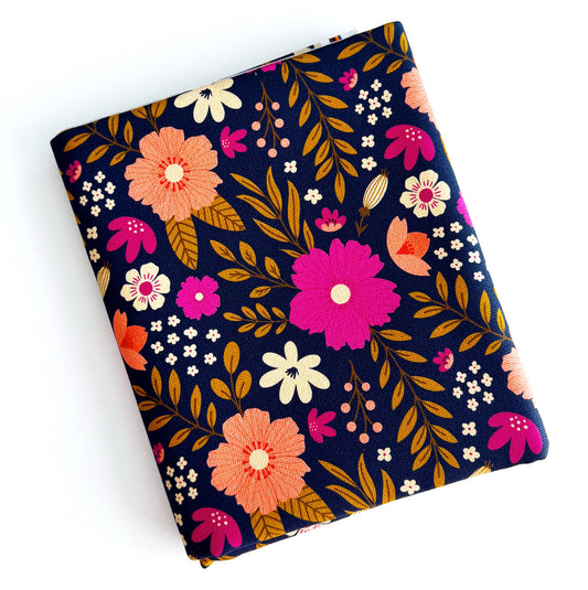 A square fabric item, likely a small pouch or sleeve, featuring a vibrant floral pattern on a dark navy blue background. The design includes large pink, orange, and cream flowers with gold-brown leaves, photographed on a clean white background.