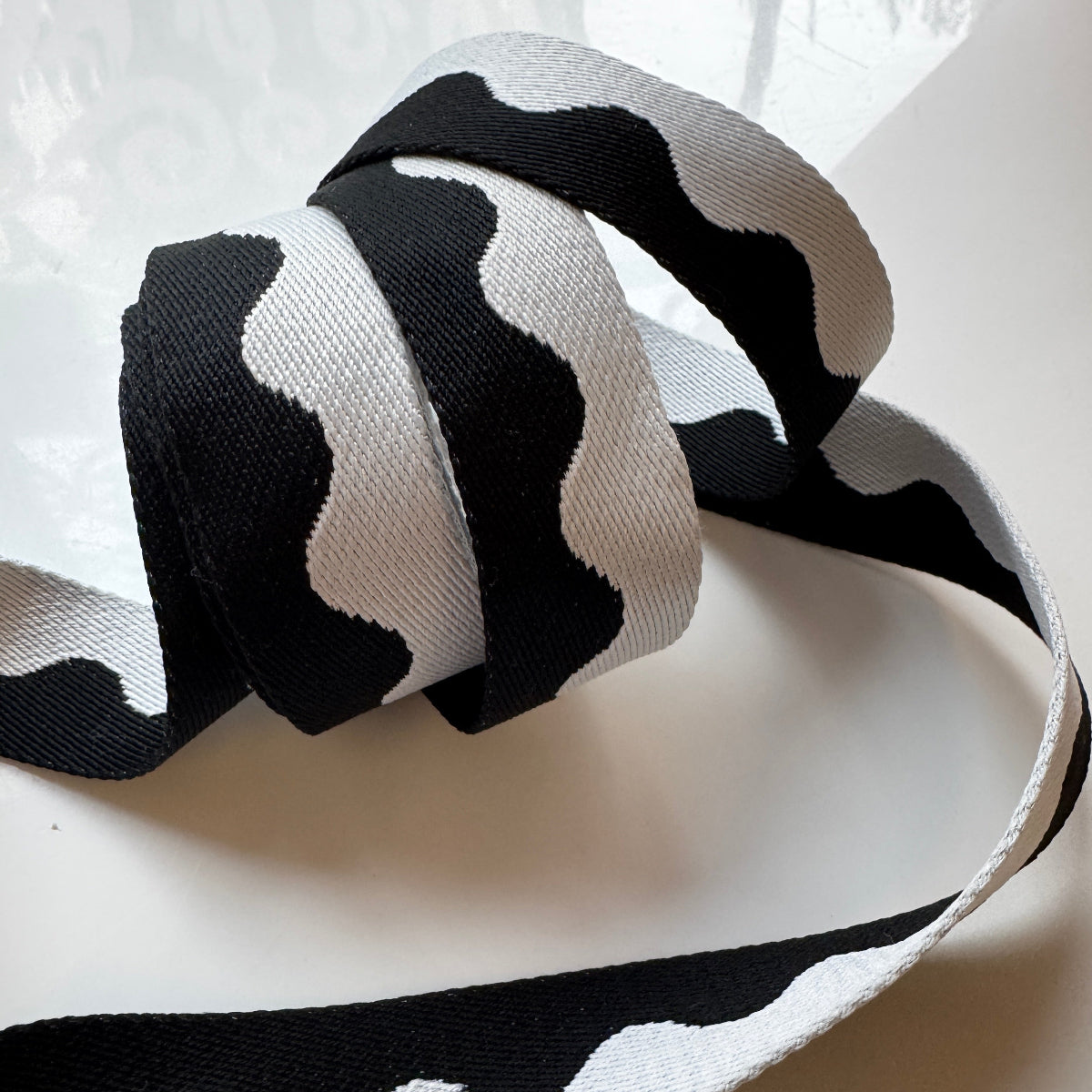 Black and white wavy patterned grosgrain ribbon, coiled and draped on a light surface.