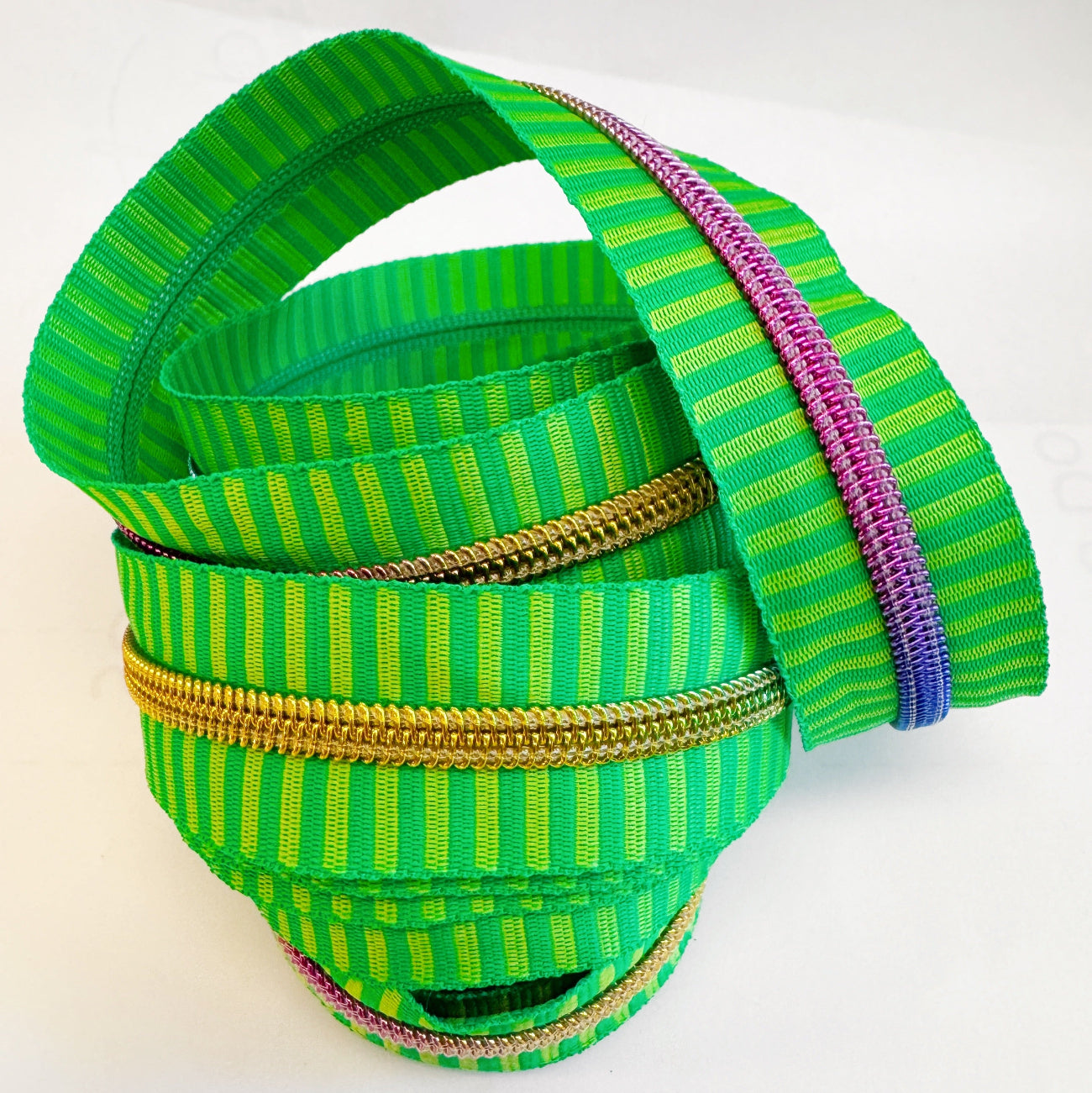 Number 5 continuous nylon coil zipper tape featuring a vibrant green and lime yellow striped jacquard woven pattern with rainbow iridescent metallic teeth, coiled against a white background.