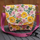 Off-white canvas messenger bag with yellow and pink floral print and pink striped crossbody strap