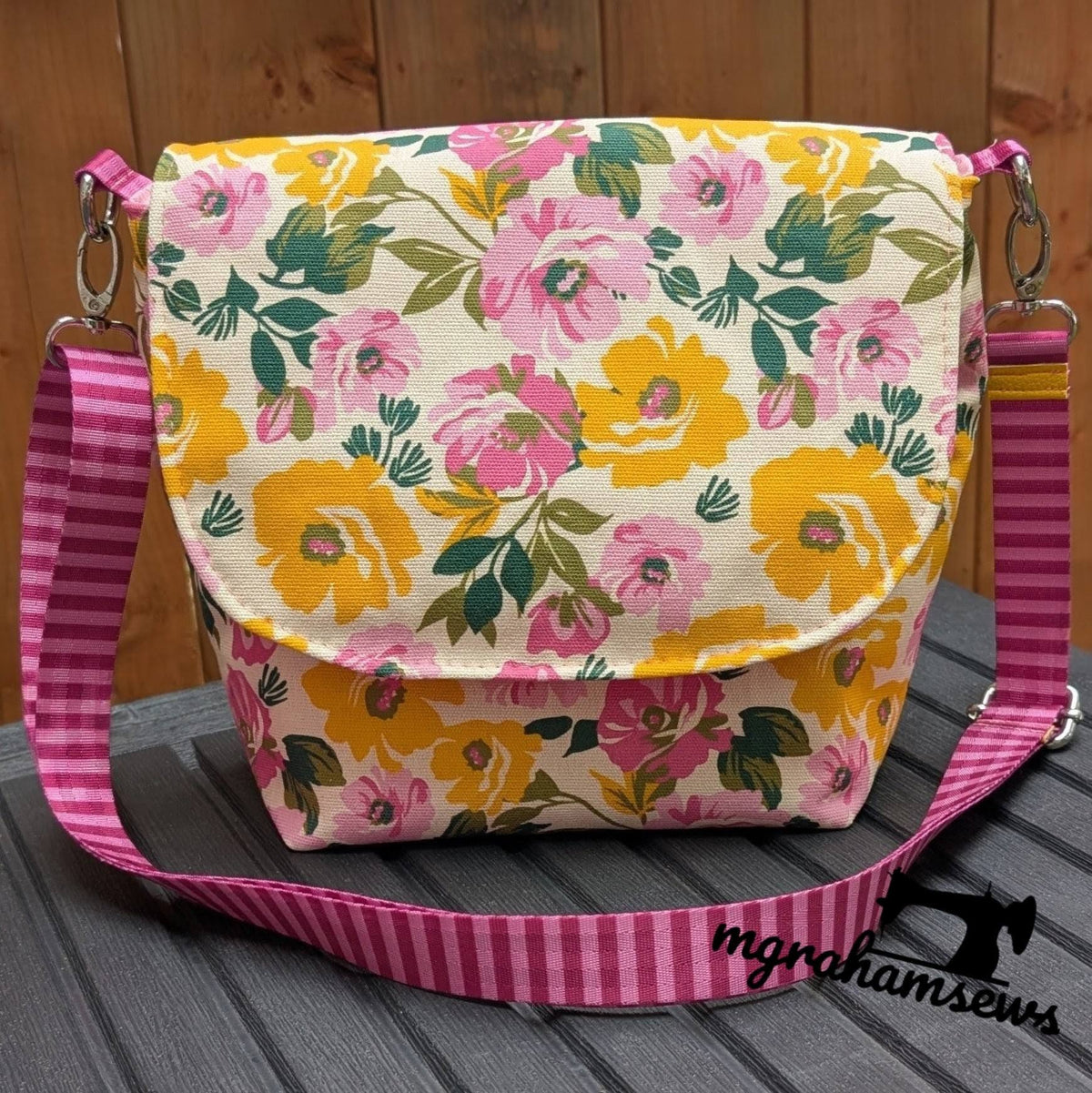 Off-white canvas messenger bag with yellow and pink floral print and pink striped crossbody strap
