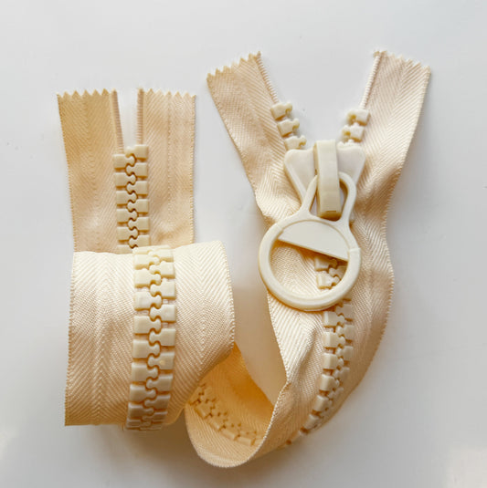 Off-white open-end resin zipper with chunky molded plastic teeth, matching round ring pull, and textured herringbone tape