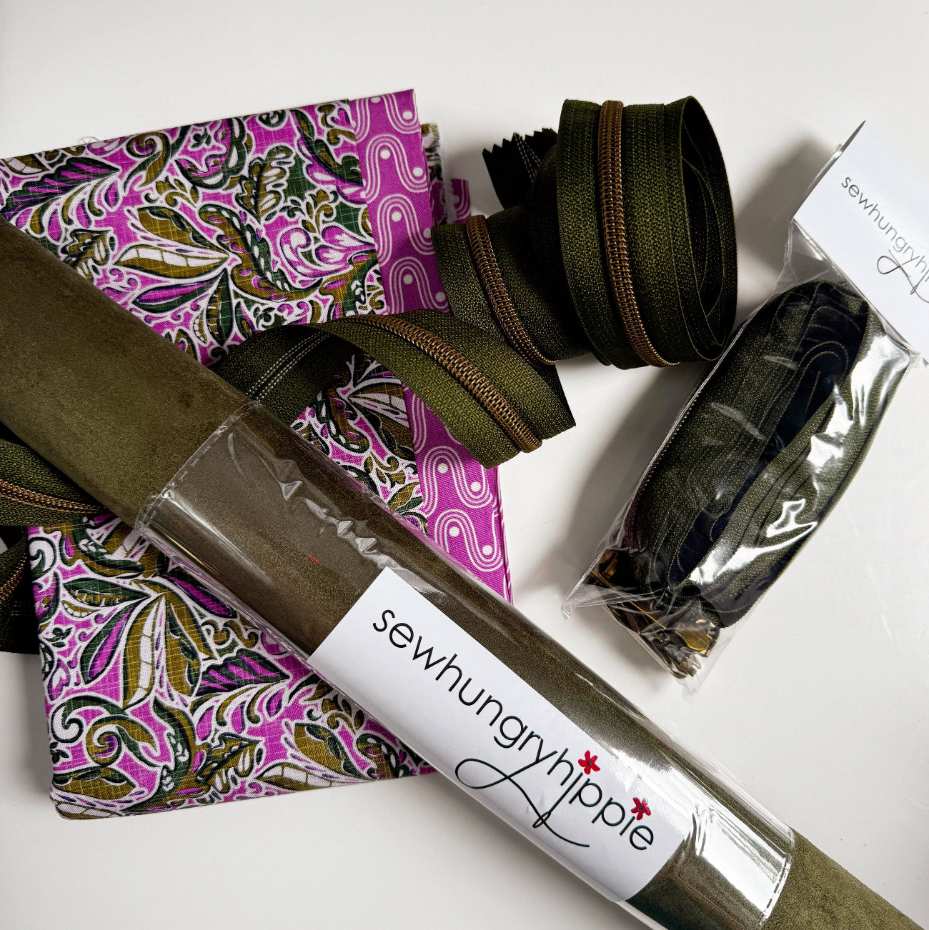 Olive suede vinyl paired with purple floral cotton fabric, coordinating zippers, and bag hardware for sewing handbags, crossbody bags, and handmade accessories.