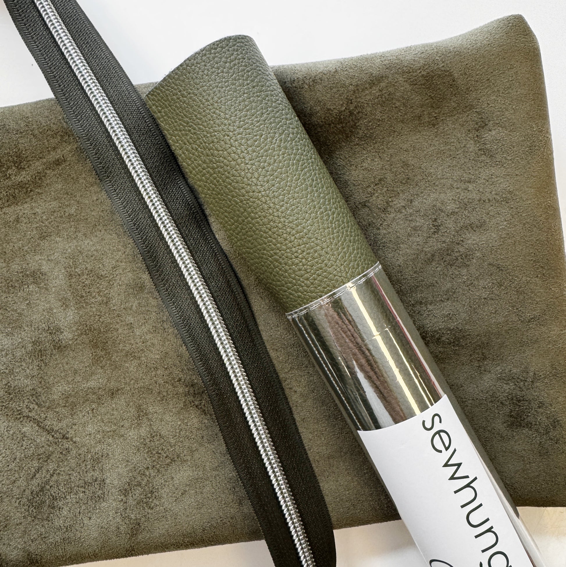 Green leather roll with a silver zipper on a textured surface, featuring the brand 'sewhung'.