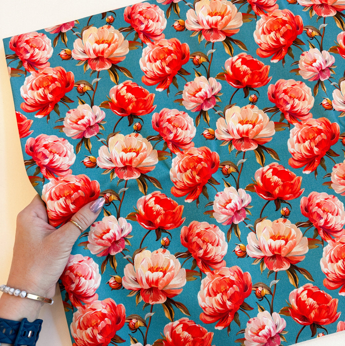 Hand holding a floral patterned paper with pink and red flowers on a blue background