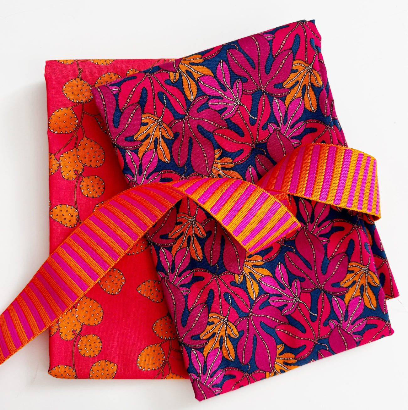 Pink floral cotton fabric paired with orange print fabric and pink-orange striped webbing for sewing handmade bags, totes, and accessories.
