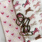 Pink horse print cotton fabric paired with coordinating heart print fabric and antique brass bag hardware for sewing handbags, crossbody bags, totes, and handmade accessories.