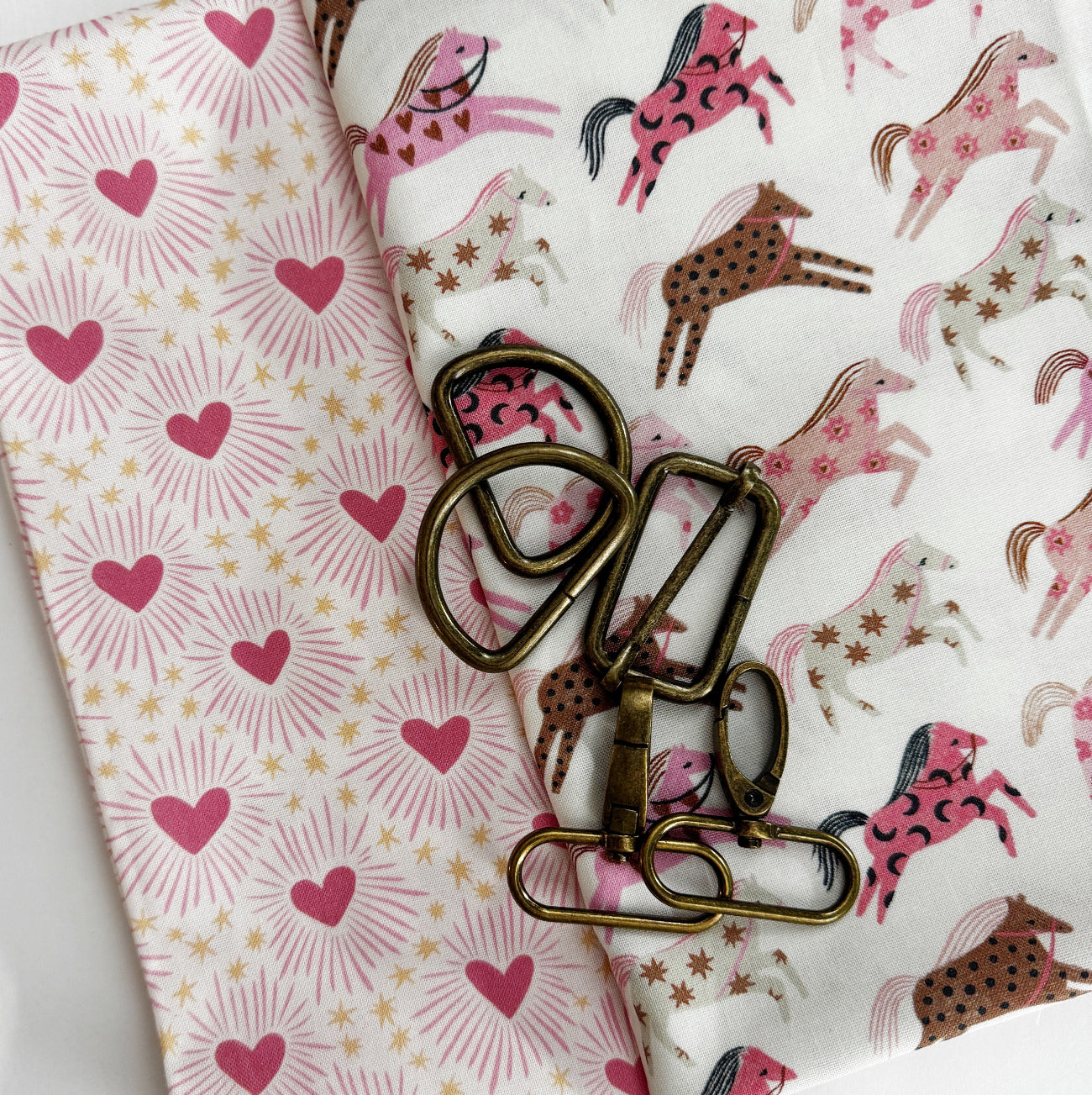 Pink horse print cotton fabric paired with coordinating heart print fabric and antique brass bag hardware for sewing handbags, crossbody bags, totes, and handmade accessories.