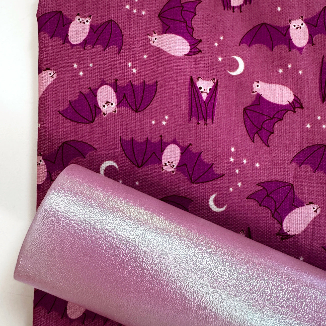 Pink iridescent vinyl paired with purple bat print cotton fabric for sewing Halloween bags, wallets, and handmade accessories.
